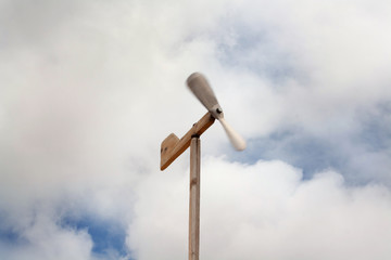 Wooden weather vane in the form of a plane against the sky and clouds.