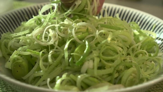 EXTREME CLOSE UP Male chef mixing sliced leeks with oil, salt and pepper. Healthy concept.
