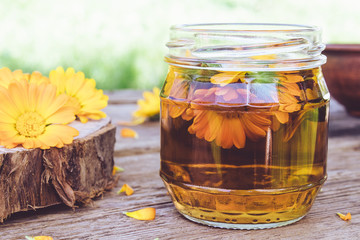 Transparent jar of calendula tincture with a fresh plant of calendula officinalis. Extract of tincture of calendula.