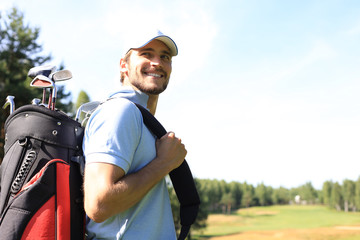 Golf player walking and carrying bag on course during summer game golfing.