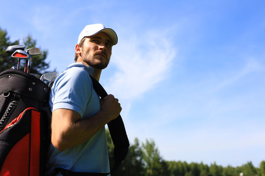 Portrait of male golfer carrying golf bag while walking by green grass of golf club.