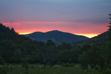 Sunset behind a mountain through the forest