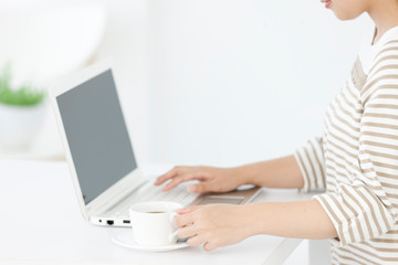 コーヒーを飲みながらパソコンを操作する女性
