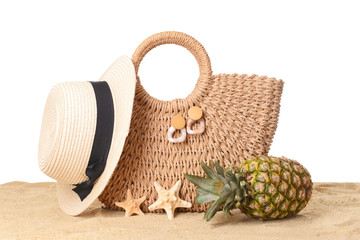 Beach bag and accessories on sand against white background