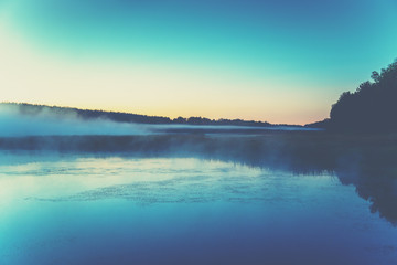 The magical foggy sunrise over the lake. Rural landscape. Summer landscape in the early morning