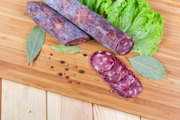 Top view of partly sliced dry-cured sausage, greens, spices