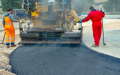 Worker regulate tracked paver laying asphalt heated to temperatures above 160 ° pavement on a...