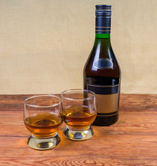 Two glasses and bottle of brandy on a rustic table