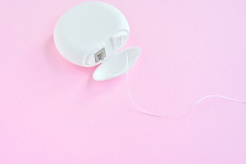 Dental floss in white plastic box with selective focus on pink background with empty space for image or text. White hygienic dental floss for daily routine healthcare on neutral backdrop