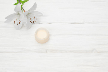 Facial cream in a jar and a lily flower on a white wooden table background with a copy space.