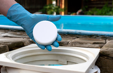 Female hand puts white tablets into pool skimmer. Cleaning, disinfection of water in the swimming...