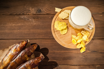 Oktoberfest holiday concept. Beer, smoked fish, chips on a wooden textural background in a dark key. Beer in a glass, fish in paper close-up and copy space.