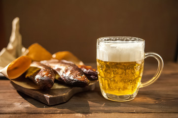 Oktoberfest holiday concept. Beer, smoked fish, chips on a wooden textural background in a dark key. Beer in a glass, fish in paper close-up and copy space.