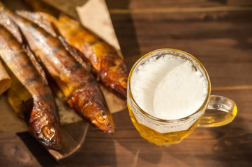 Oktoberfest holiday concept. Beer, smoked fish, chips on a wooden textural background in a dark key. Beer in a glass, fish in paper close-up and copy space.
