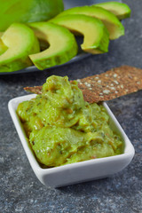 Guacamole in a bowl on a background of sliced avocado.