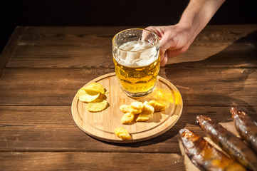 Oktoberfest holiday concept. Beer, smoked fish, chips on a wooden textural background in a dark key. Beer in a glass, fish in paper close-up and copy space.