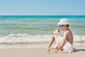 Fototapeta na wymiar Child boy with dog jack russel on beach. Best friends rest on vacation, play in sand against sea. Tourism and vacation on ocean. Family vacation in summer. Vacation at sea with dog. Summer travel
