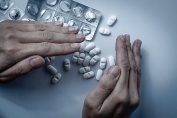 Hands covers and hiding many white prescription drugs, medicine tablets or vitamin pills in a pile - Concept of healthcare, opioids addiction, shame, medicament abuse or medication treatment