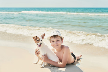 Child boy with dog jack russel on beach. Best friends rest on vacation, play in sand against sea. Tourism and vacation on ocean. Family vacation in summer. Vacation at sea with dog. Summer travel