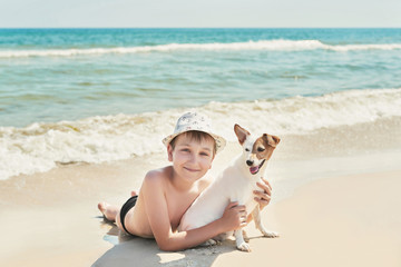 Child boy with dog jack russel on beach. Best friends rest on vacation, play in sand against sea. Tourism and vacation on ocean. Family vacation in summer. Vacation at sea with dog. Summer travel