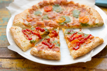 Pizza with parma ham, cheese, green pesto and tomatoes 