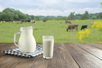 Fresh milk in glass on dark wooden table and blurred landscape with cow on meadow. Healthy eating....