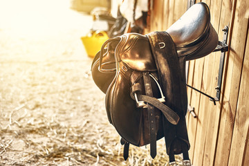 leather horse saddle in a stable hanging on the wall. - obrazy, fototapety, plakaty