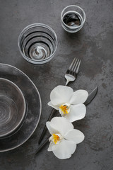 Elegance table setting with knitted grey napkin, cutlery, ceramic plates, glasses and white orchid flowers