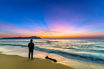 Silhouette of man on the beach looking at magical dramatic sunrise. The man standing on the sandy beach