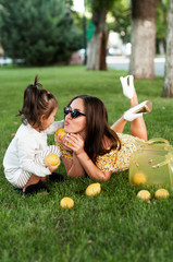 Funny mum with the daughter play with lemons lying on a grass in park..