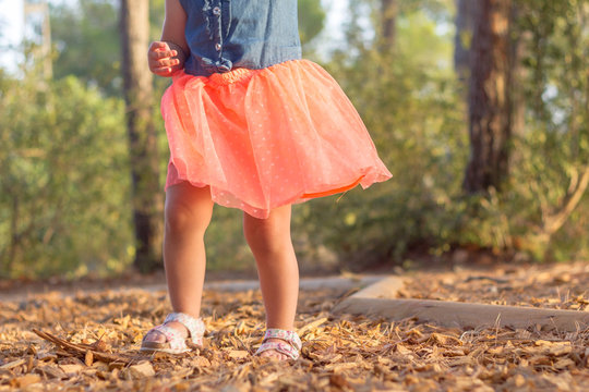 The legs of a little girl walking in the park. She is wearing a pink skirt.