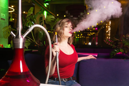 Young woman in the red dress smokes a hookan at the hookah bar. Shisha standing on the table