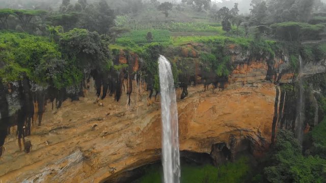 Aerial shot orbiting around sipi falls in rural Uganda as it plunges off the edge of a cliff into a deep valley.