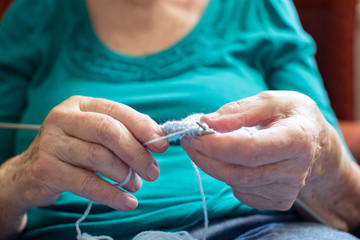 Close Up Of Senior Woman Sitting In Chair At Home And Knitting