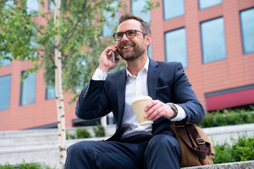 Obraz premium Mature Businessman Taking Phone Call On Mobile Sitting At Outside Office Building