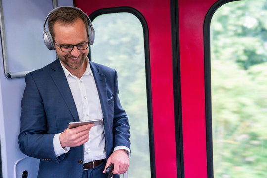 Businessman Standing On Train Streaming Movie From Mobile Phone To Wireless Headphones