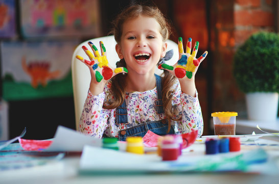 funny child girl draws laughing shows hands dirty with paint.