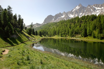 Miroir lake located above Ceillac village after one hour hike, with reflections of mountain range and pine tree forests, Queyras Regional Natural Park, Southern Alps, France