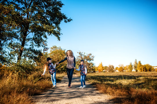 Mother and two little daughters running along the road in the autumn park