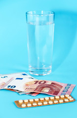 hormonal pills in yellow packaging, glass of water and euro money