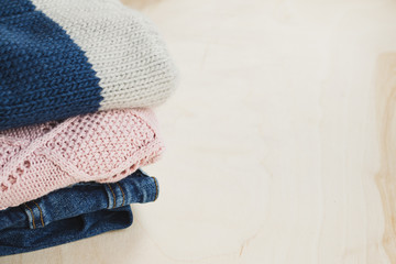 Warm clothes on a wooden table. Sweater, hat and jeans in the stack. Concept: cozy, cold season. Scandinavian style. Space for text