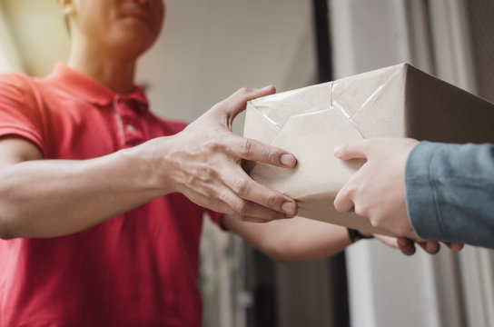 hand of young delivery service man in red uniform with woman customer receiving parcel post box from courier at home, cargo shipping, express delivery service, online shopping and logistics concept