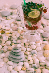 Glass with a cooling drink of berries and ice. Misted glass. Air bubbles on glass. A slice of lemon on a plate on the background of seashells.