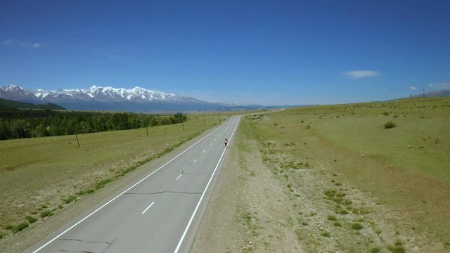 Aerial photography of traveling girl with backpack on an asphalt road on sunny day among the mountains. Panoramic view from the height of road extending into the distance among the mountain. Beautiful