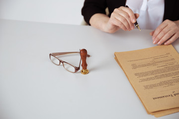 Notary woman writing by pen on a paper. Attorney concept. Glasses and stamp