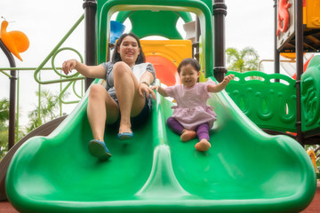 Asian mother and daughter are happiness and enjoy playing slide equipment together in playground, with fully happiness moment.