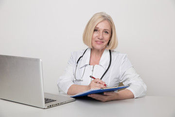 Woman doctor in a white medical clothes sitting in cabinet and working on a laptop