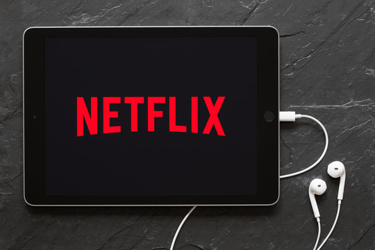 Riga, Latvia - March 25, 2018: Earphones connected to iPad showing Netflix logo on the screen.