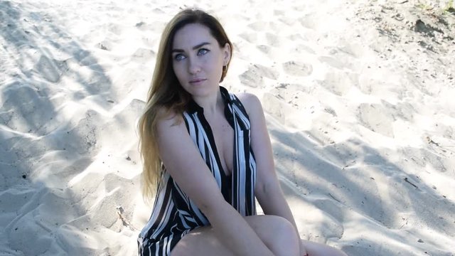 Young brunette girl in black swimsuit sitting on the beach in the sand.