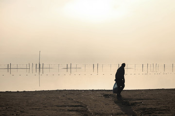 Silhouette of a man cleaning a lake beach at sunrise